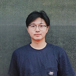 Portrait of man with black hair, glasses and blue shirt against gray background.