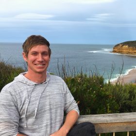 Man in striped gray sweatshirt at a beach.