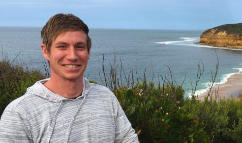 Man in striped gray sweatshirt at a beach.