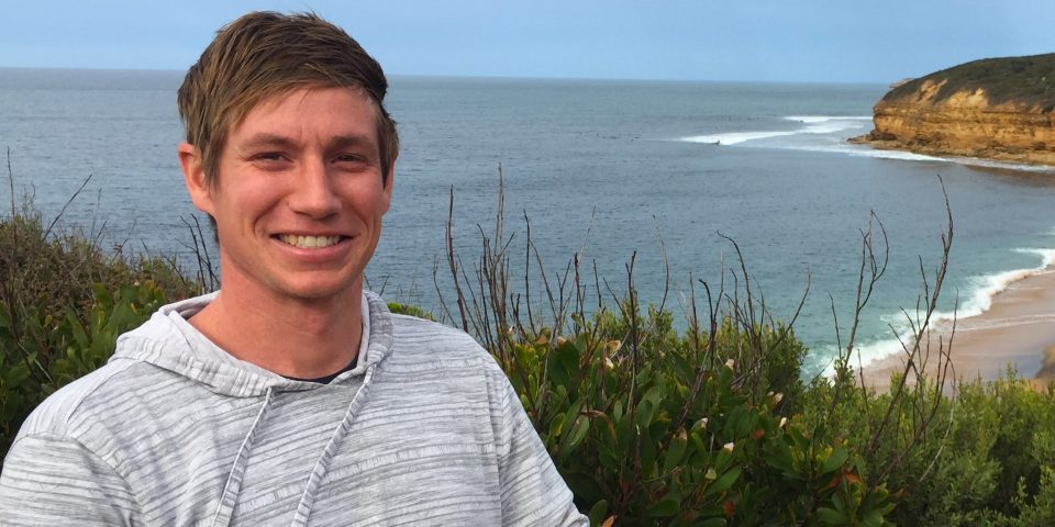 Man in striped gray sweatshirt at a beach.